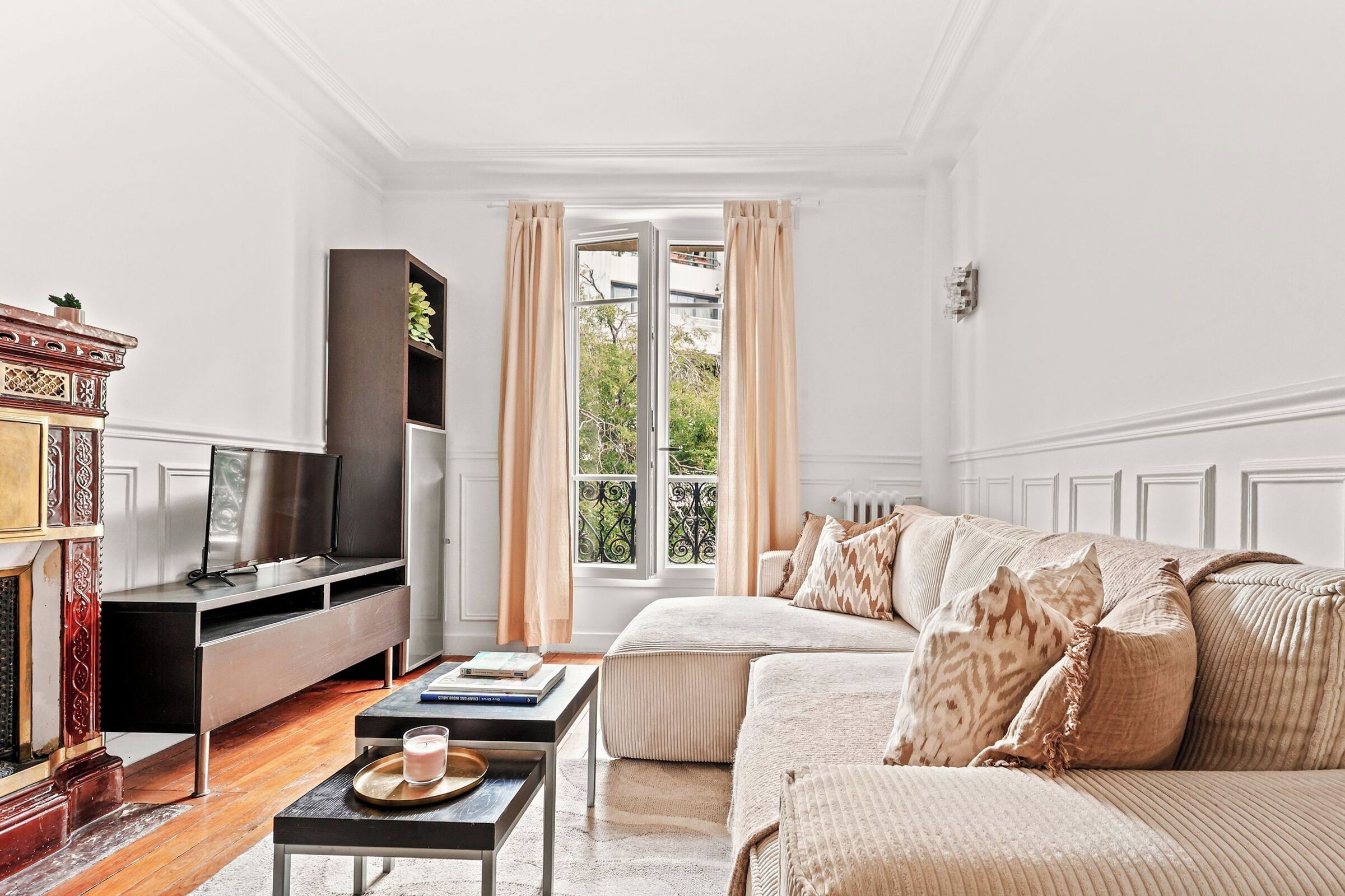 A well-lit living room with a sofa, a television, a fireplace, and a window with curtains.