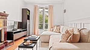 Uma sala de estar bem iluminada com sofá, televisão, lareira e janela com cortinas.