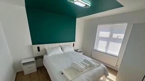 Un dormitorio moderno con una cama grande, mesitas de noche, un velador, una ventana con persianas y una lámpara en el techo.