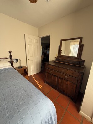 Quarto com cama, penteadeira, espelho e porta que dá para um corredor.