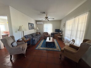 Un salon comprenant un canapé, des fauteuils, une table basse, un téléviseur et un ventilateur de plafond.