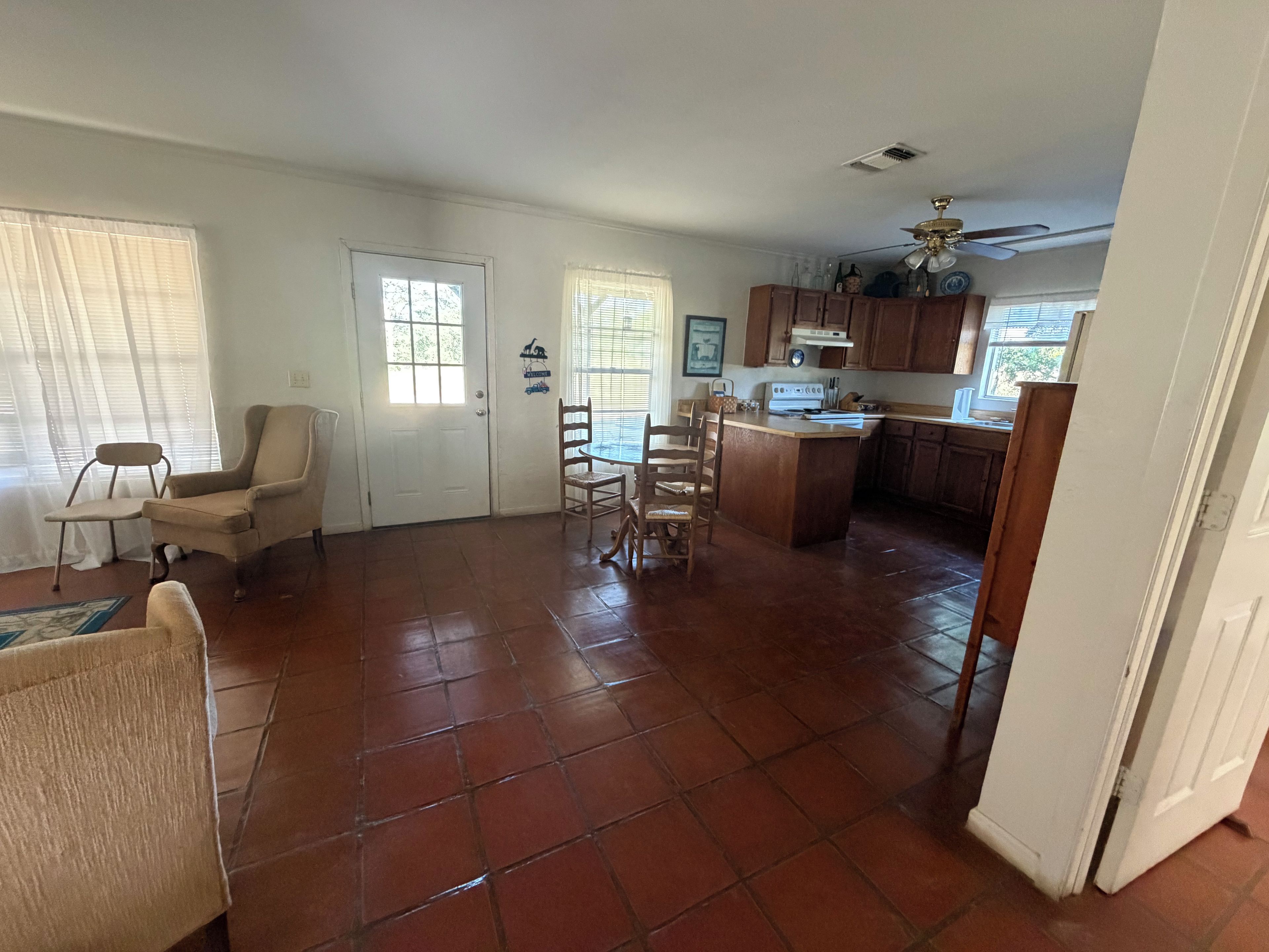 A spacious living area with a dining set, a kitchen with wooden cabinets, and a door leading to another room.