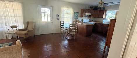 A spacious living area with a dining set, a kitchen with wooden cabinets, and a door leading to another room.