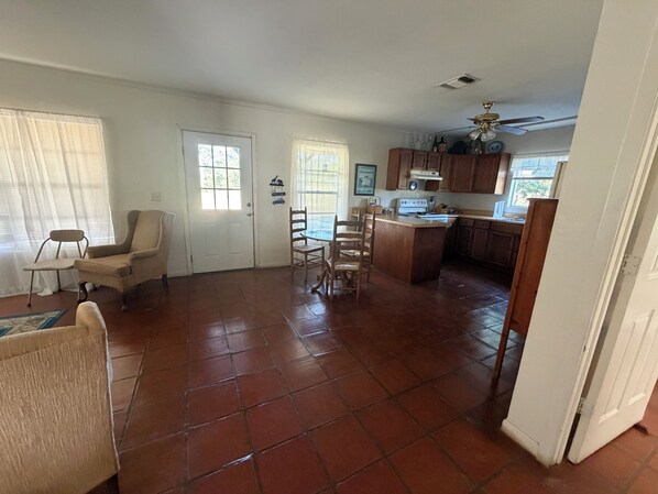 A spacious living area with a dining set, a kitchen with wooden cabinets, and a door leading to another room. - Cute and Cozy 2 room cottage on the Medina River. (Bandera)