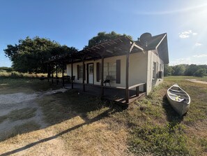 A small house with a porch, a canoe, and a picnic table. - Cute and Cozy 2 room cottage on the Medina River. (Bandera)