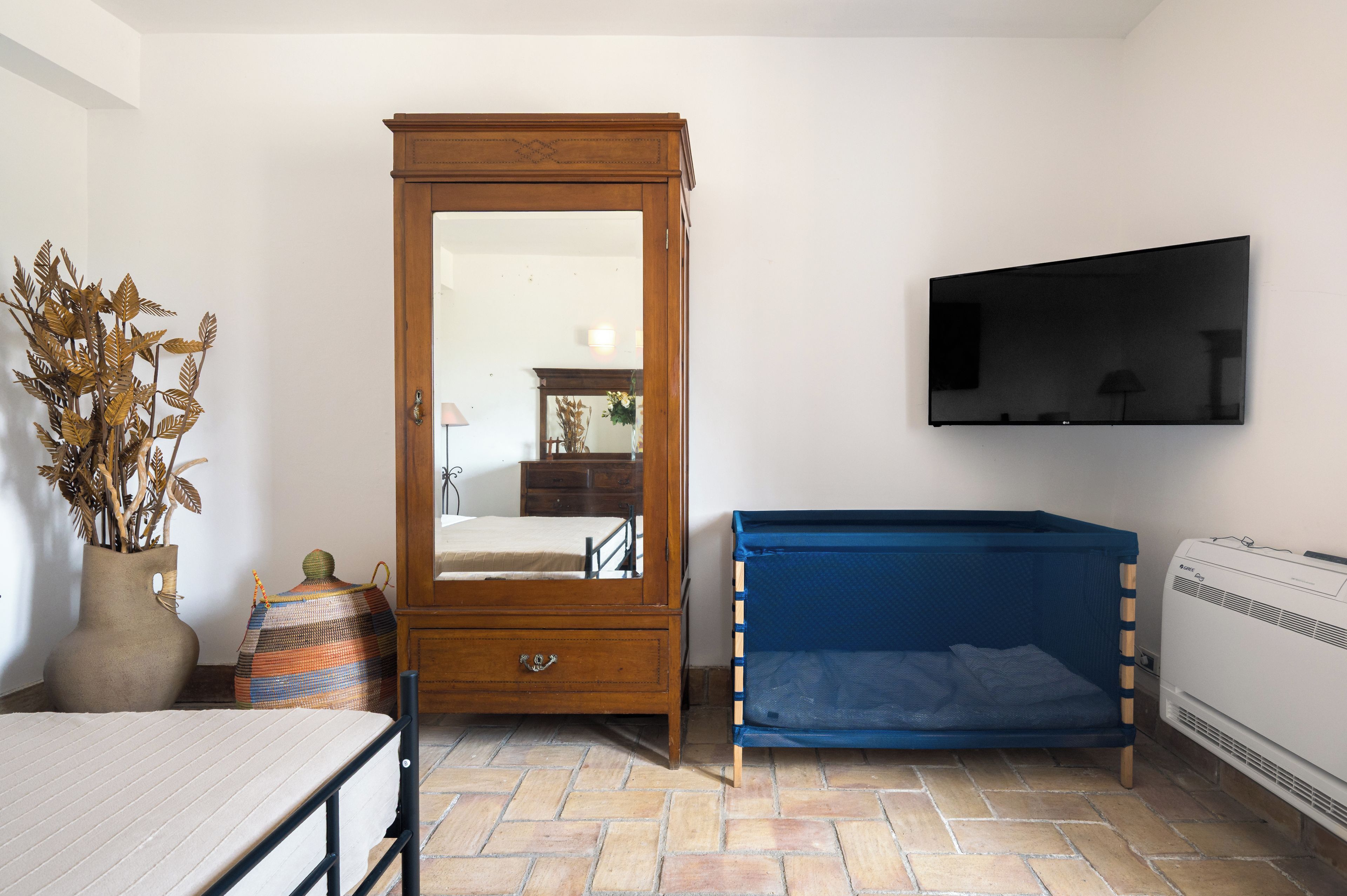 Une chambre avec une armoire en bois, un lit avec un matelas bleu, un téléviseur fixé au mur et un radiateur.