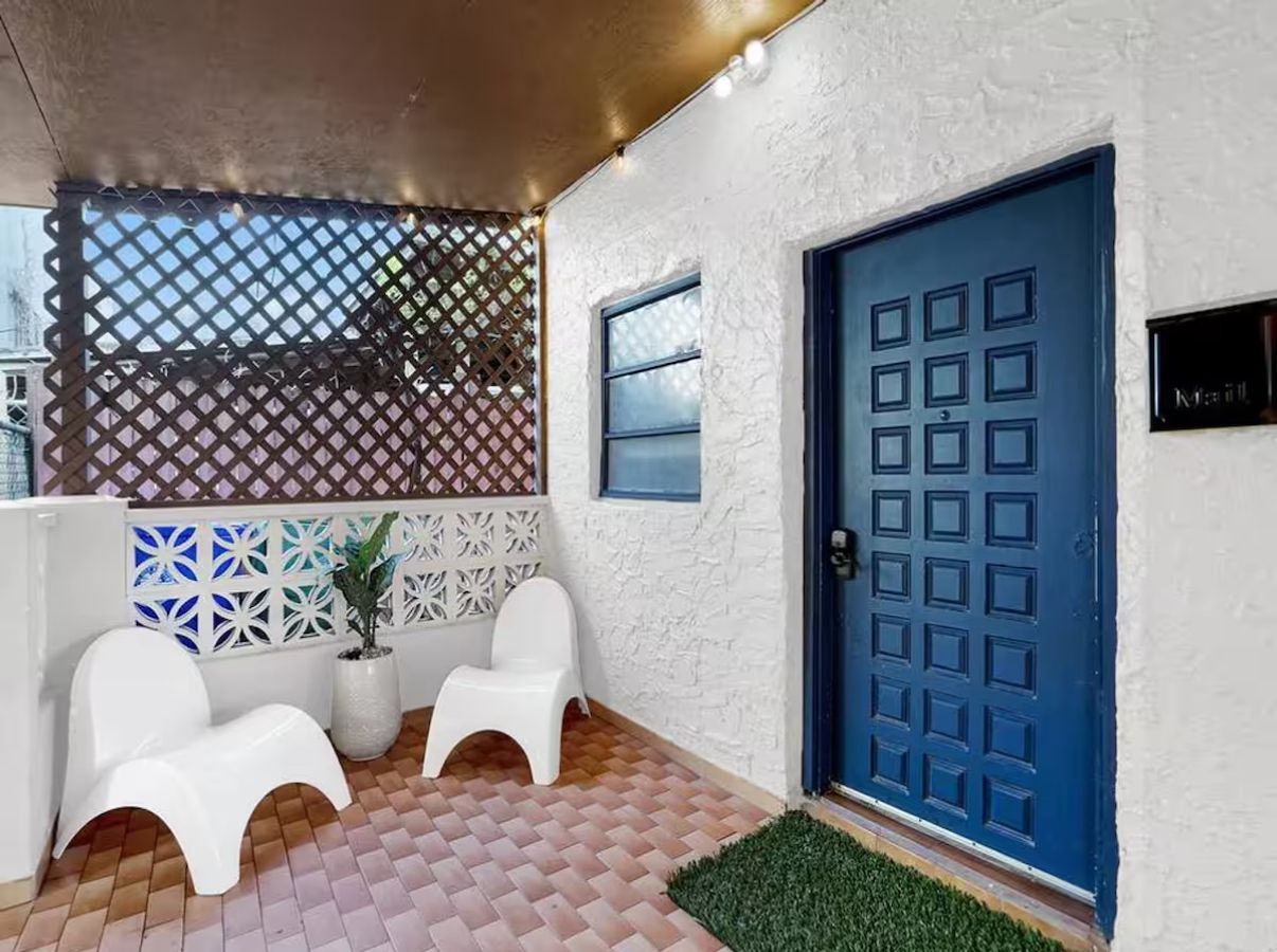 Una habitación con puerta azul, paredes blancas y suelo estampado.