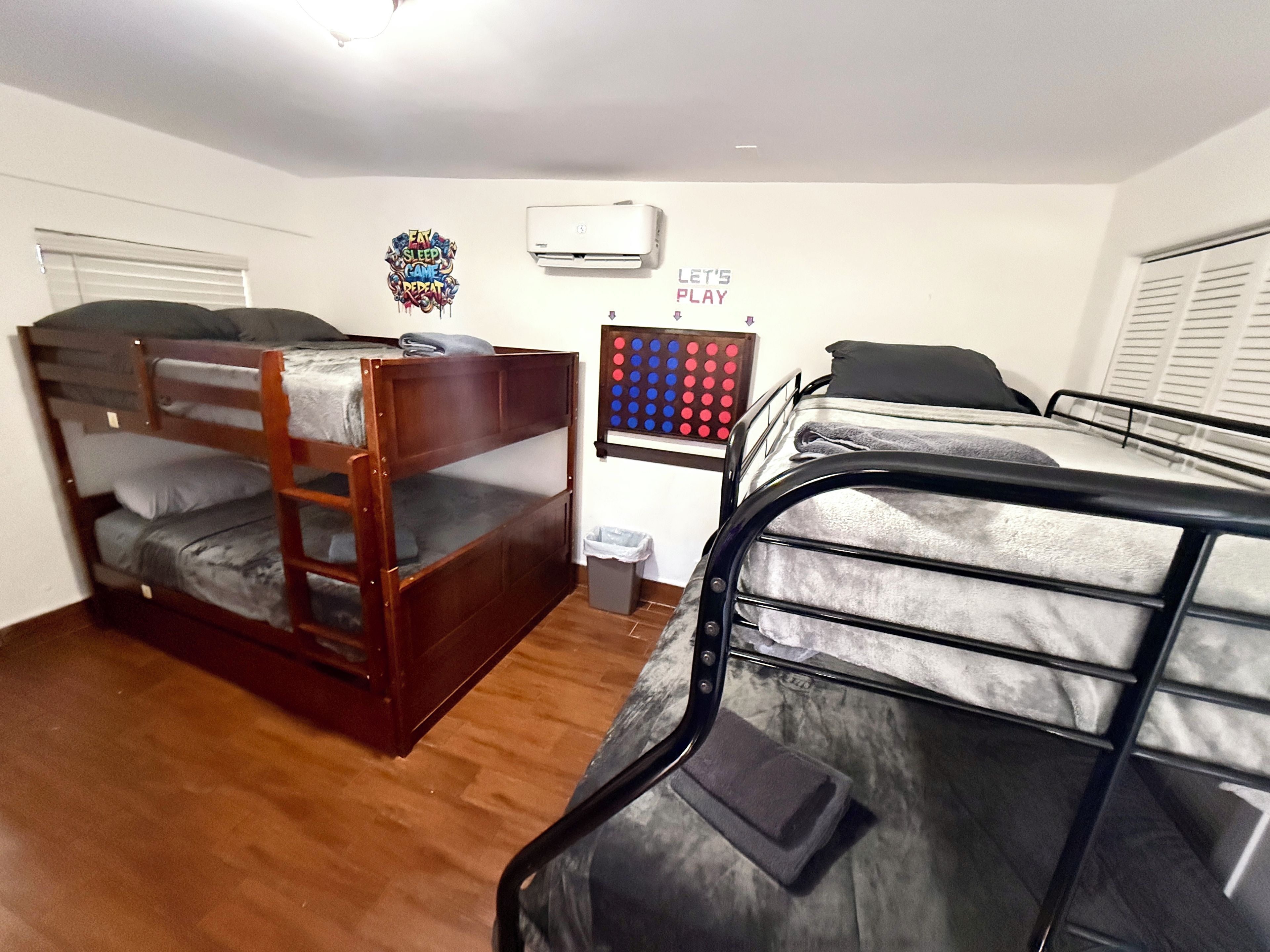 Ein Zimmer mit Etagenbetten, einer Wandklimaanlage, einem Korkbrett und einem Fenster mit Jalousien.