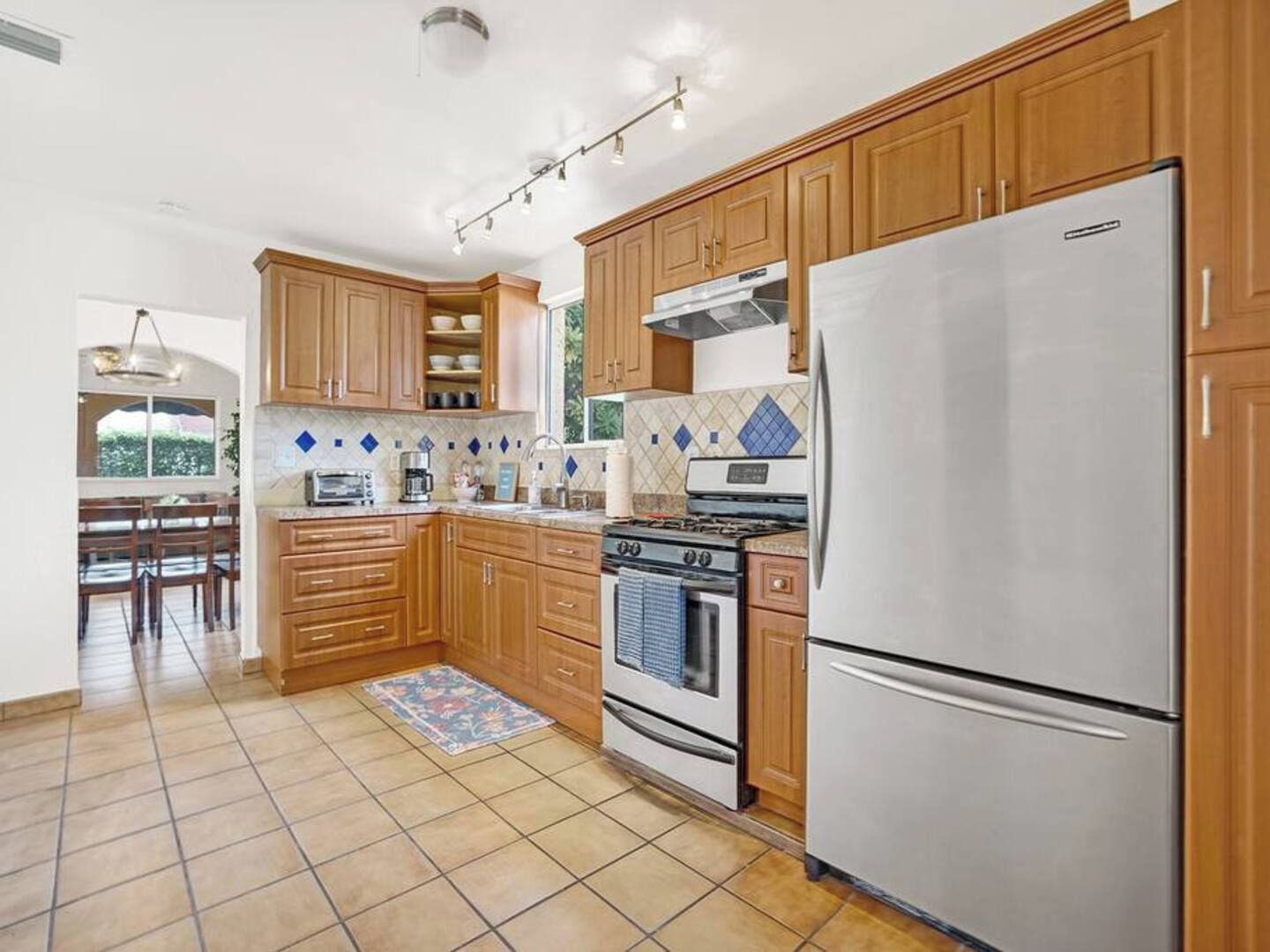 Una cocina con armarios de madera, un refrigerador de acero inoxidable, una estufa a gas y un revoque de azulejos.