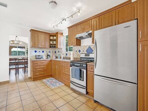 Una cocina con armarios de madera, un refrigerador de acero inoxidable, una estufa a gas y un revoque de azulejos.