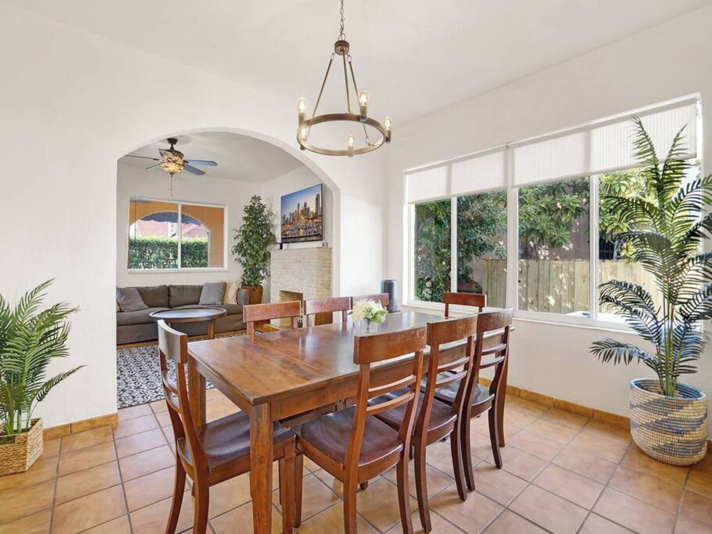 Un comedor con mesa y sillas de madera, una araña y vistas a un jardín a través de amplios ventanales.