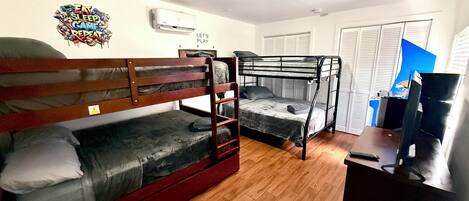 A dormitory room with bunk beds, a desk, a chair, and a television.