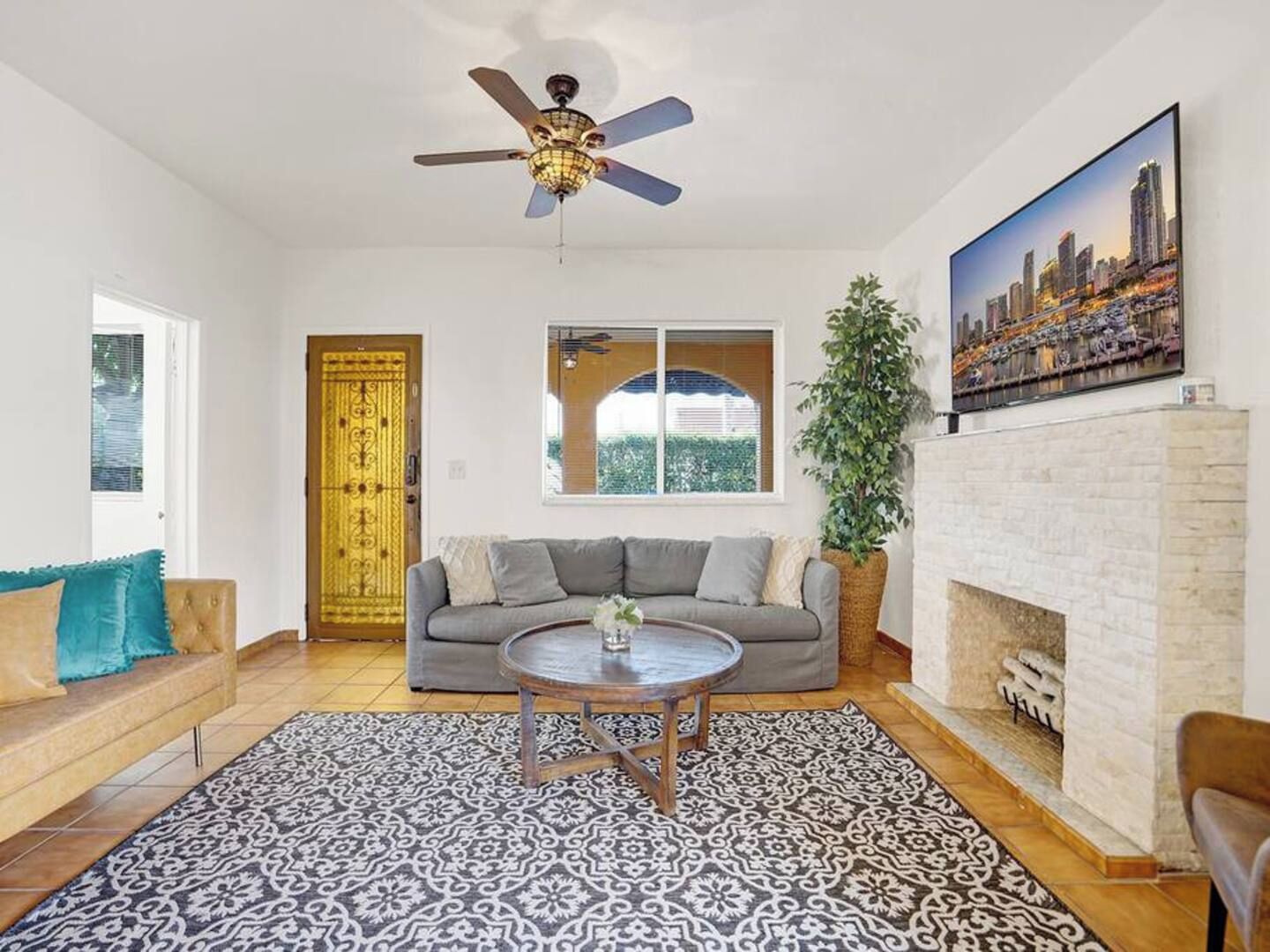 Una sala de estar con un sofá, una mesa de centro, una chimenea, un ventilador de techo y una pintura de un paisaje urbano.