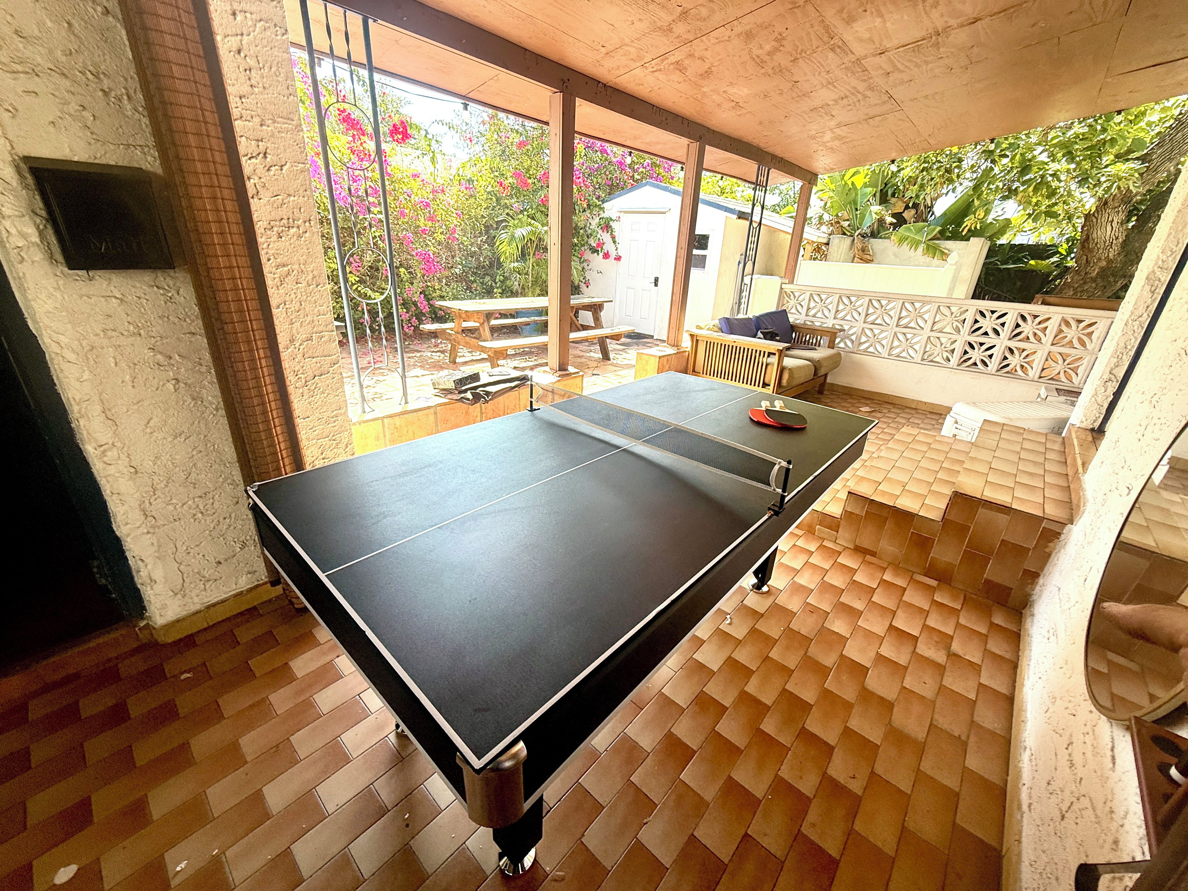 Ein Tischtennis-Tisch in einem Raum mit Fliesenboden und Blick auf einen Garten durch große Fenster.