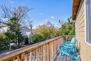Eine Holzterrasse mit Geländer, ein blauer Adirondack-Sessel und Blick auf ein Haus und Bäume.