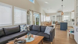 A spacious living room with a grey sectional sofa, a wooden coffee table, and a dining area with a wooden table and chairs. - Pet-Friendly, 5 min walk to beach & ferry (Ocean Beach)
