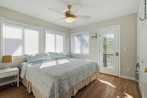 Un dormitorio con cama, mesita de noche, ventilador de techo y puerta con ventanal.