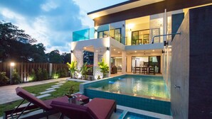 Una casa moderna de dos pisos con piscina, mobiliario exterior y un jardín bien cuidado.