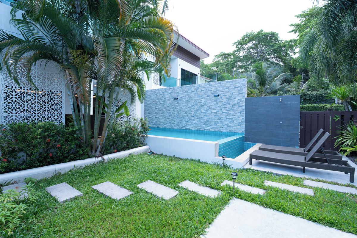 Un área de piscina moderna al aire libre con pared de piedra, sillones de descanso y una cerca decorativa.