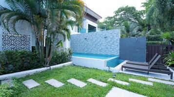 Un área de piscina moderna al aire libre con pared de piedra, sillones de descanso y una cerca decorativa.