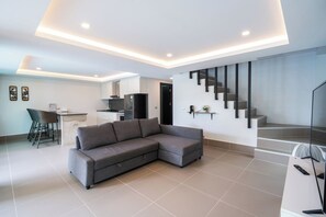 A modern living room with a sectional sofa, a dining area with a chair, and a staircase. - Neau Melo Private Luxury Pool Villa (Ko Chang District)