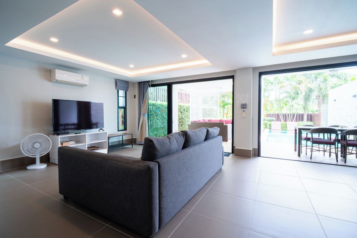 A modern living room with a sofa, TV, and fan, leading to a patio with outdoor furniture.