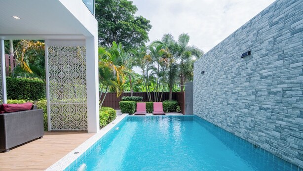 Una piscina con dos sillas de descanso, una pared blanca y una valla decorativa.