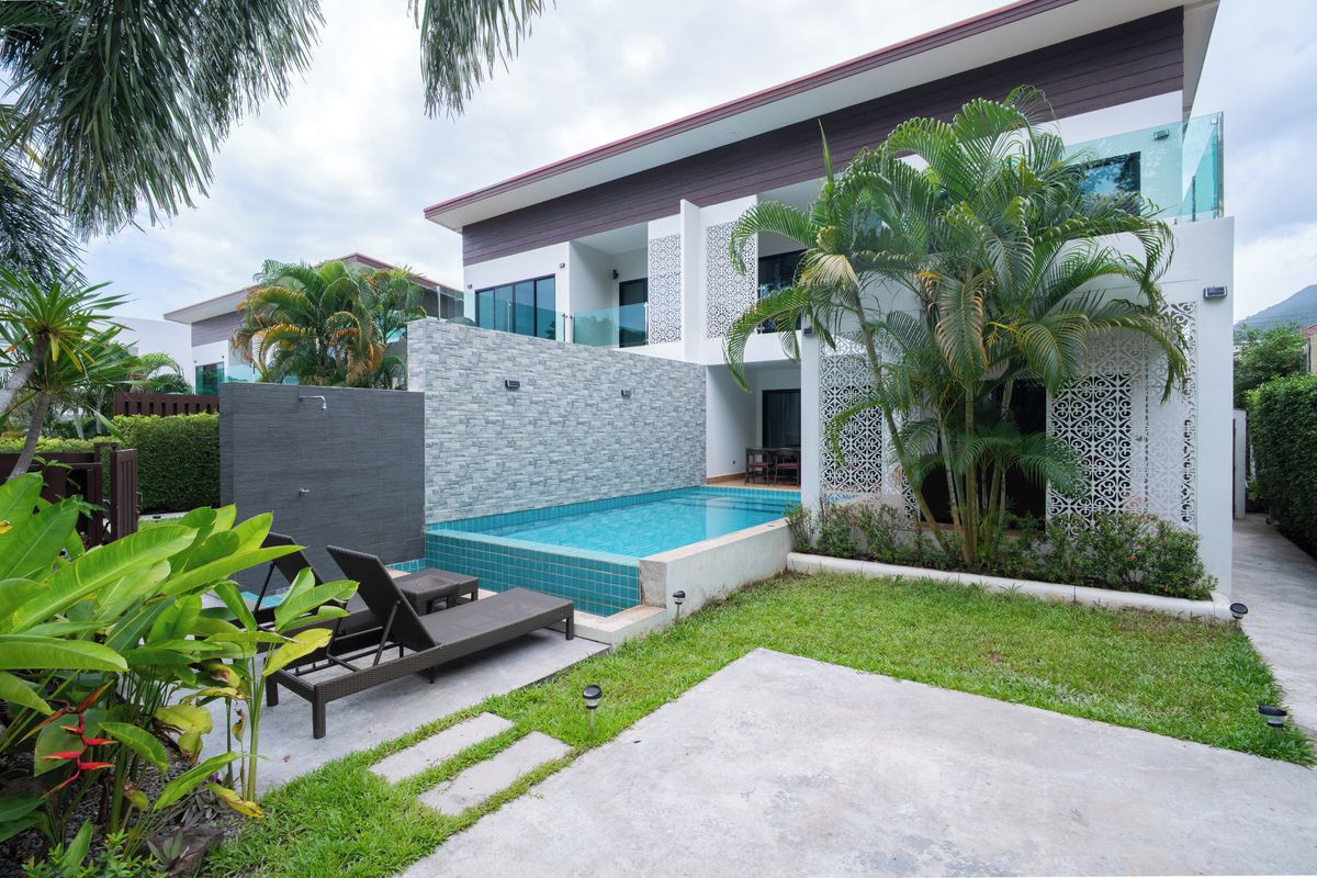 Un edificio moderno de dos pisos con piscina, mobiliario exterior y plantas tropicales.