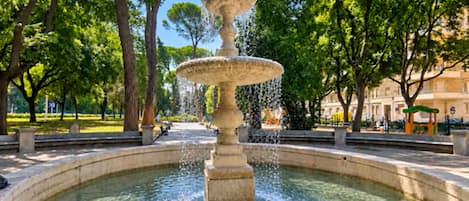 A multi-tiered fountain in a circular stone basin surrounded by trees.