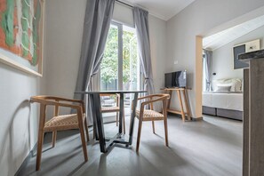 Una habitación con una mesa, sillas, un televisor sobre un mueble bajo y una cama con cabecera.
