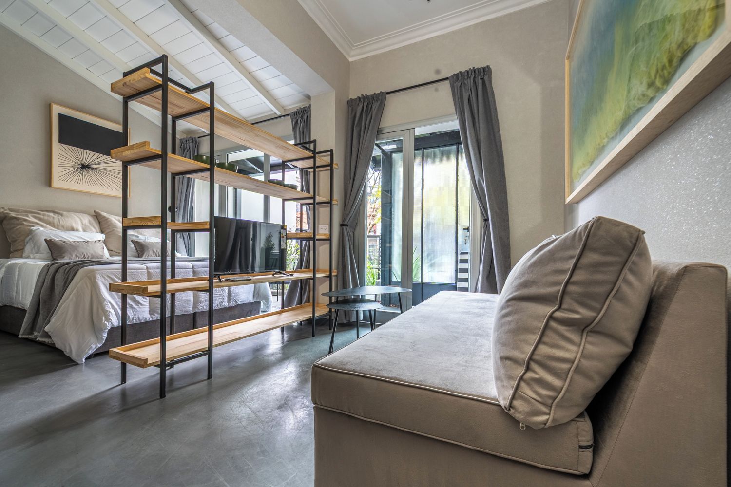 A modern bedroom with a sofa, a TV on a wooden shelf, a bed, and a window with curtains.
