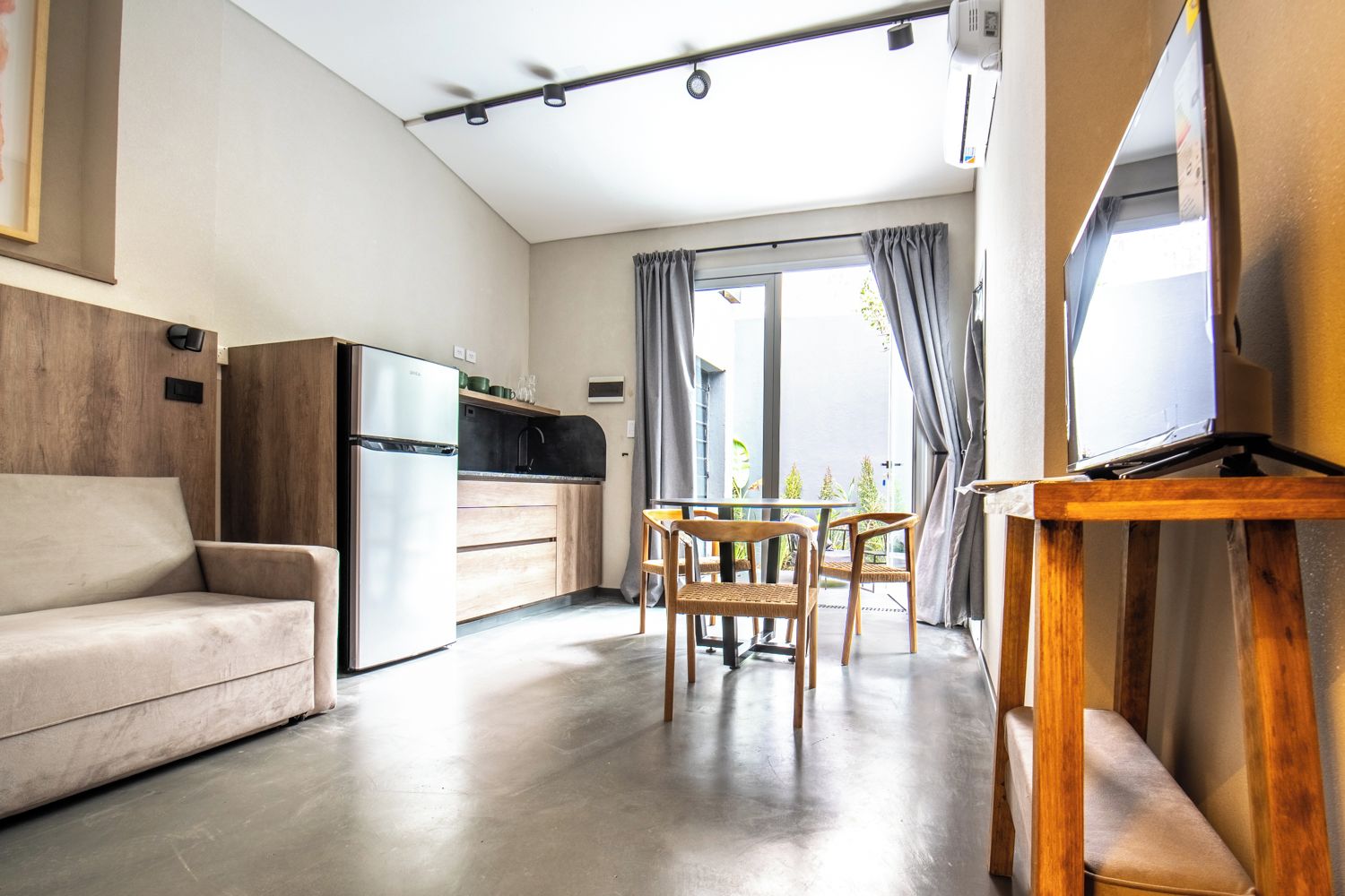 A modern living room with a sofa, a dining table with chairs, a kitchen area, and a television on a stand.