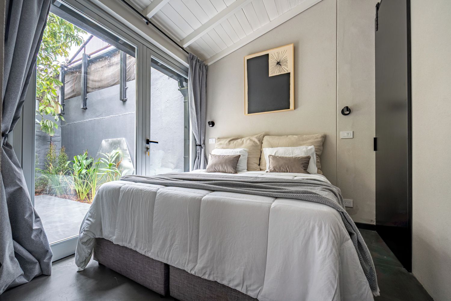 Un dormitorio con una cama grande, una puerta corrediza de vidrio a un balcón y un cuadro en la pared.