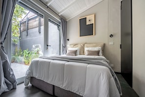 A bedroom with a large bed, a sliding glass door to a balcony, and a framed picture on the wall.