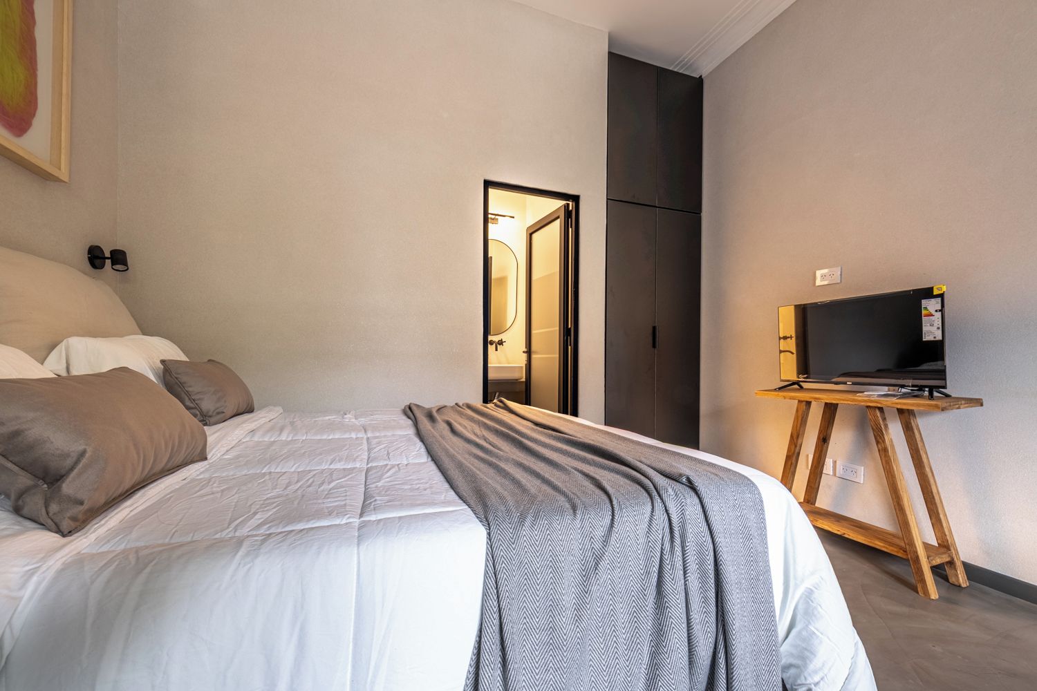 A hotel room with a bed, a television on a wooden stand, and a wardrobe.