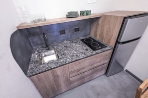 A compact kitchen with a granite countertop, a stainless steel sink, a built-in stove, and a refrigerator.