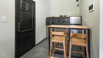 Una cocina compacta con una puerta negra, una mesita con dos sillas, un refrigerador y un televisor.
