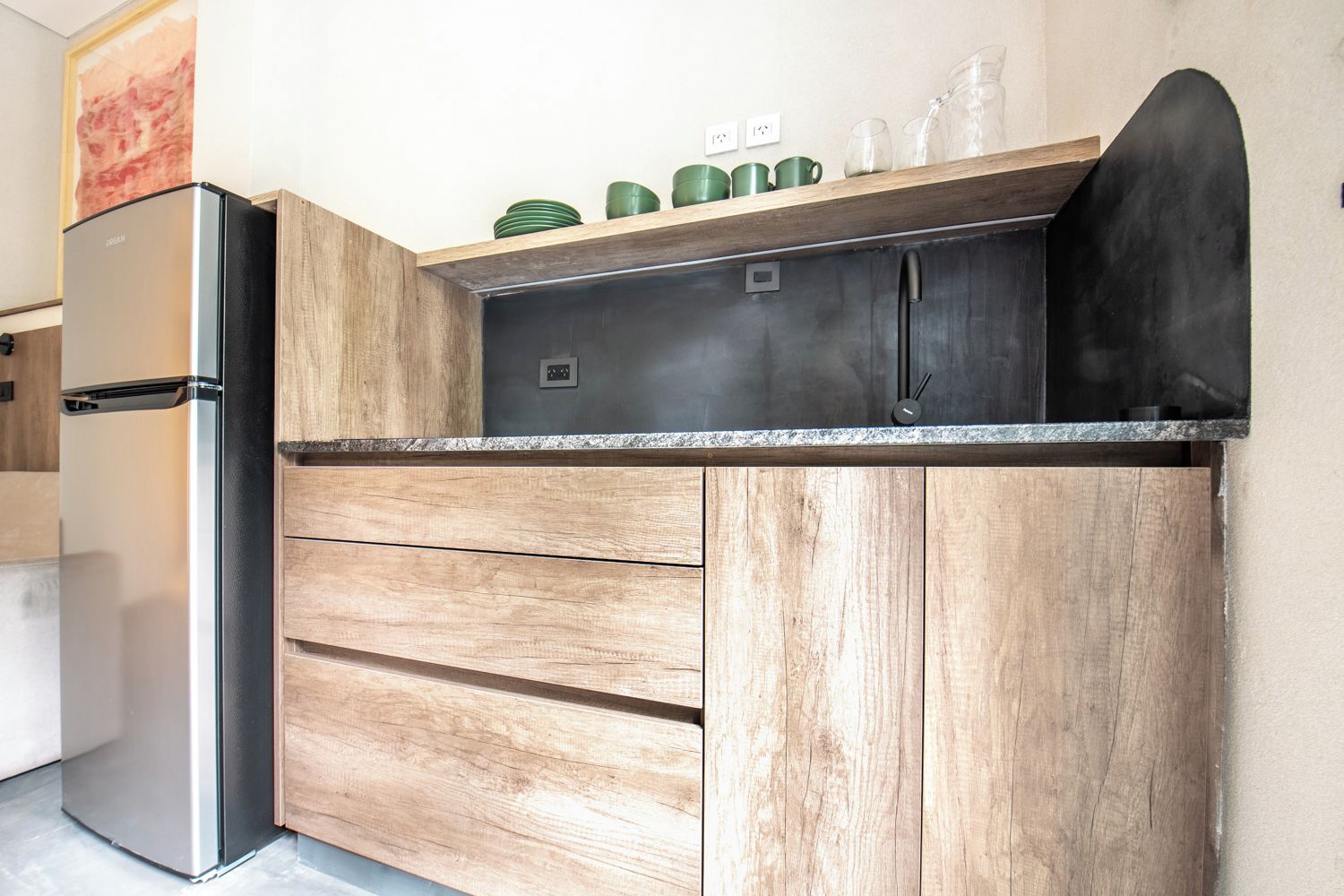 Eine Küche mit einem Edelstahl-Kühlschrank, Holzschränken und einer Arbeitsplatte mit grünen Tassen und Gläsern.