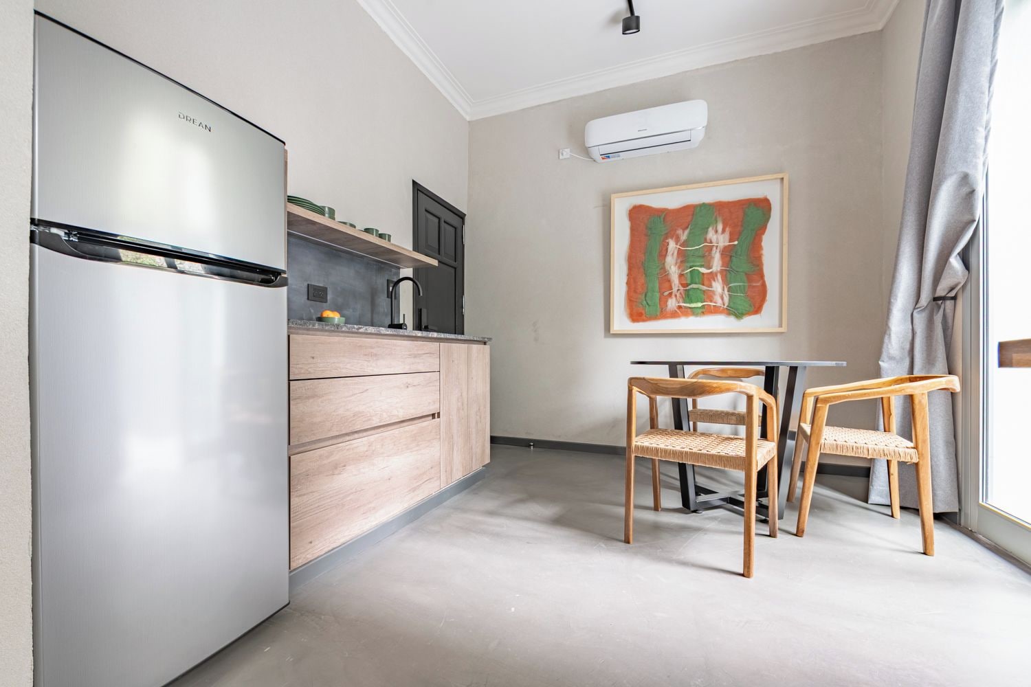 Una cucina compatta con un frigorifero moderno, mobili in legno e un’area pranzo con due sedie.