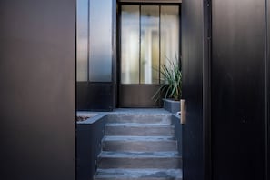 A modern staircase leading to a door with a metal gate, flanked by dark walls and a potted plant.
