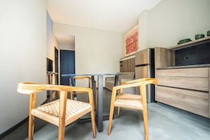 A compact kitchen with two wooden chairs, a dining table, a refrigerator, and a wooden cabinet.