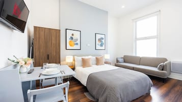 Ett modernt hotellrum med en säng, en soffa, ett skrivbord med en stol, en TV som är monterad på väggen och två inramade konstverk.
