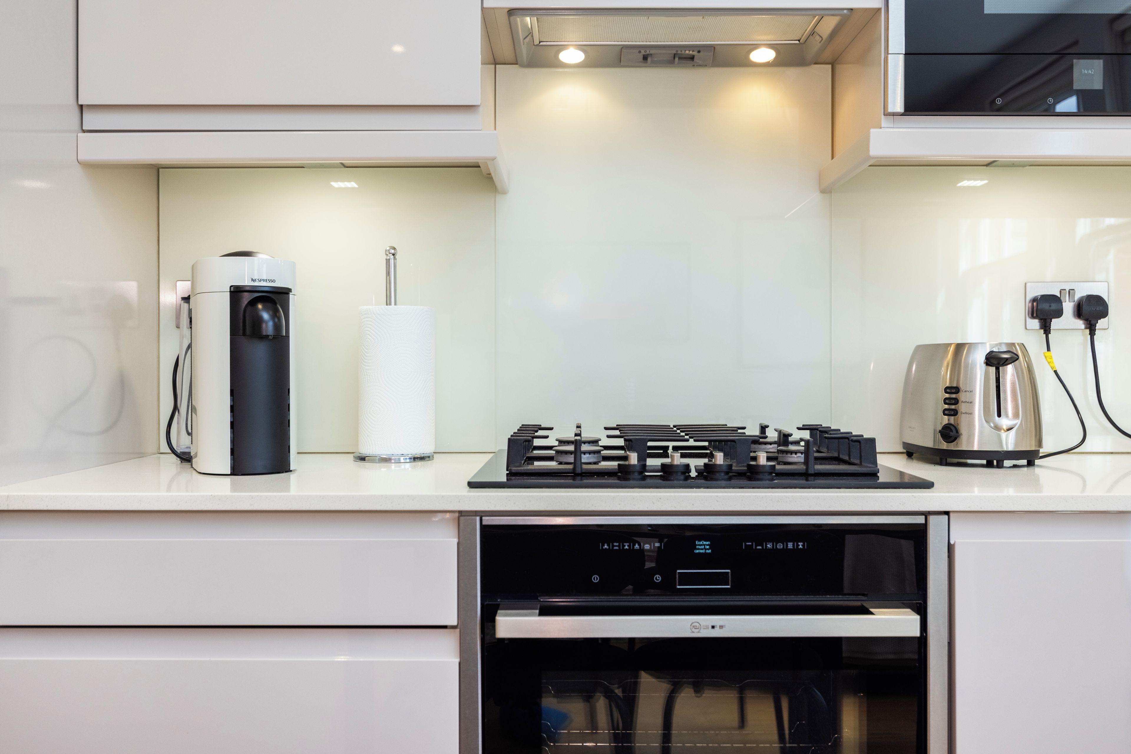 A modern kitchen with a built-in espresso machine, a paper towel dispenser, a toaster, and a stove.