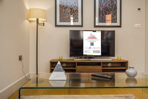 Una sala de estar moderna con una mesa de centro de vidrio, un control remoto, un jarrón y un televisor sobre un mueble de madera.