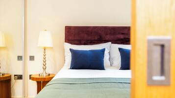 Una habitación de hotel con una cama, una mesita de noche, una lámpara y una puerta con manija.