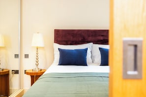 Una habitación de hotel con una cama, una mesita de noche, una lámpara y una puerta con manija.