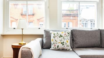 Een kamer met een bank, een lamp en uitzicht op gebouwen door een raam.