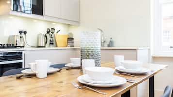 Een moderne keuken met witte kasten, een houten eettafel gedekt met witte borden, kommen en kopjes.