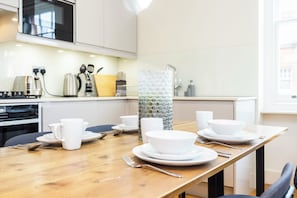 Una cocina moderna con armarios blancos, una mesa de comedor de madera dispuesta con platos, tazones y tazas blancos.