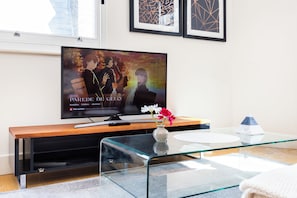 Una sala de estar moderna con un televisor de pantalla plana sobre un mueble de madera, una mesa de centro de vidrio y un jarrón con flores.